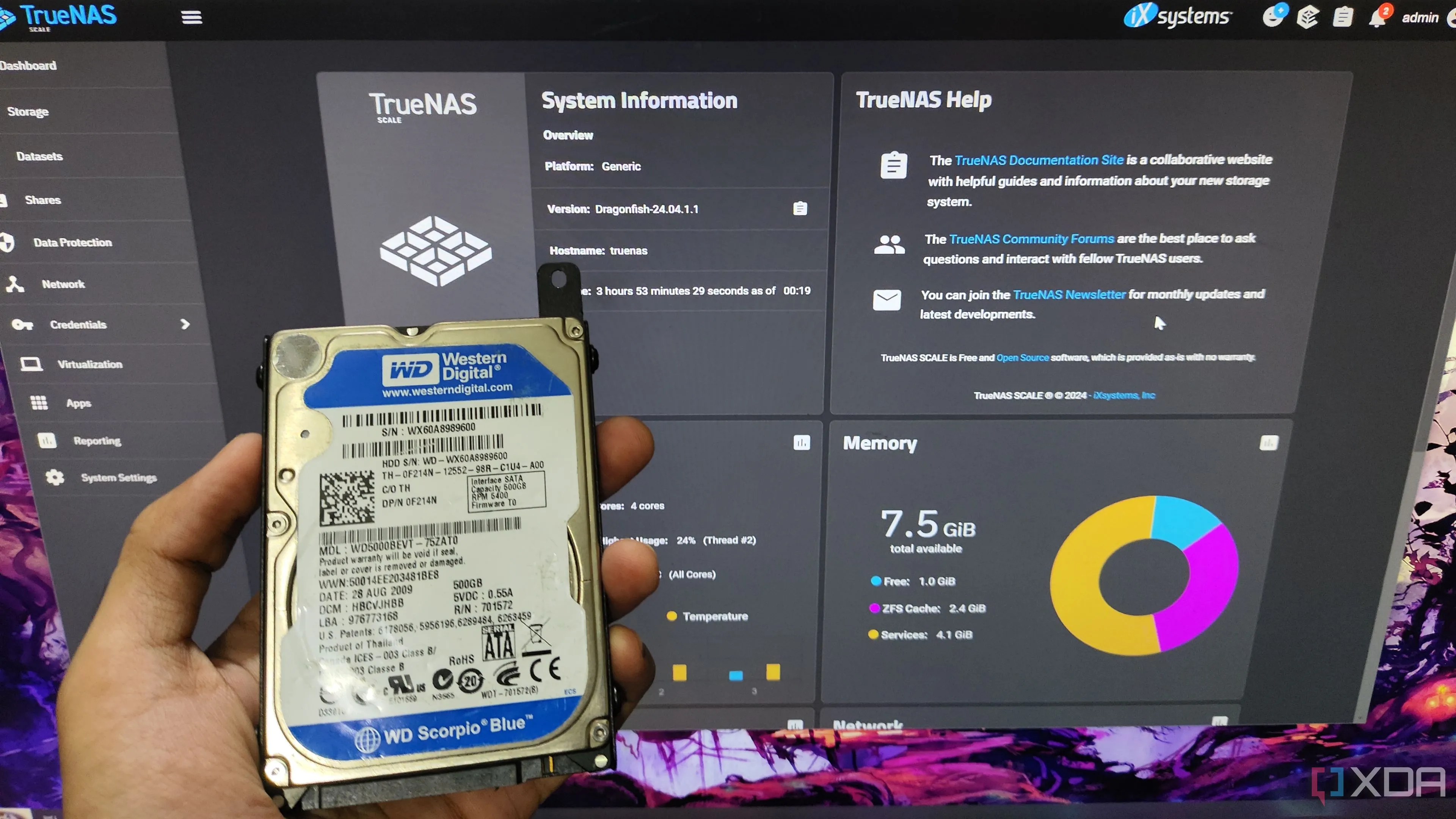 Một người đang cầm ổ cứng HDD trước màn hình hiển thị giao diện quản lý TrueNAS, cho thấy vai trò trung tâm của HDD trong hệ thống NAS tự xây dựng