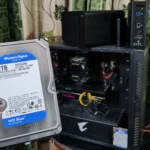 Người dùng cầm ổ cứng HDD trước máy tính và hai thiết bị NAS TerraMaster