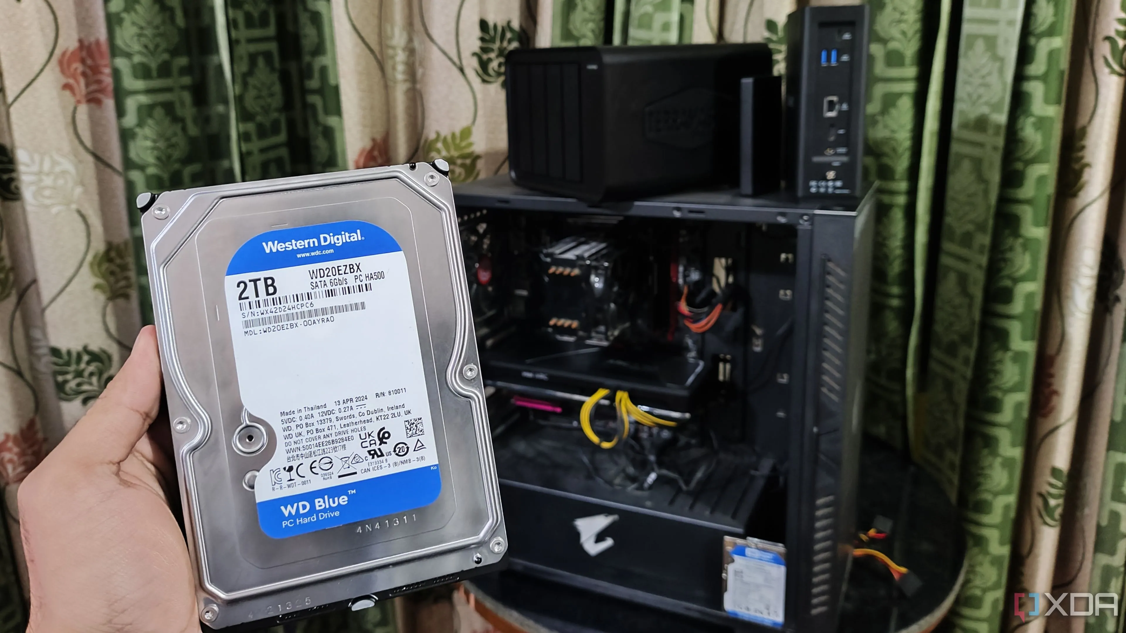 Người dùng cầm ổ cứng HDD trước máy tính và hai thiết bị NAS TerraMaster