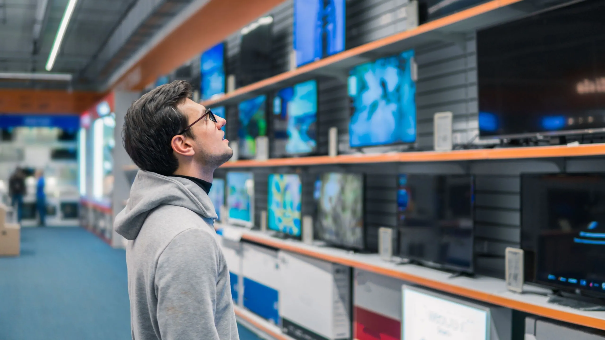 Người đàn ông đang xem các mẫu TV 4K thông minh tại cửa hàng điện tử, cân nhắc lựa chọn cho trải nghiệm xem phim UHD.