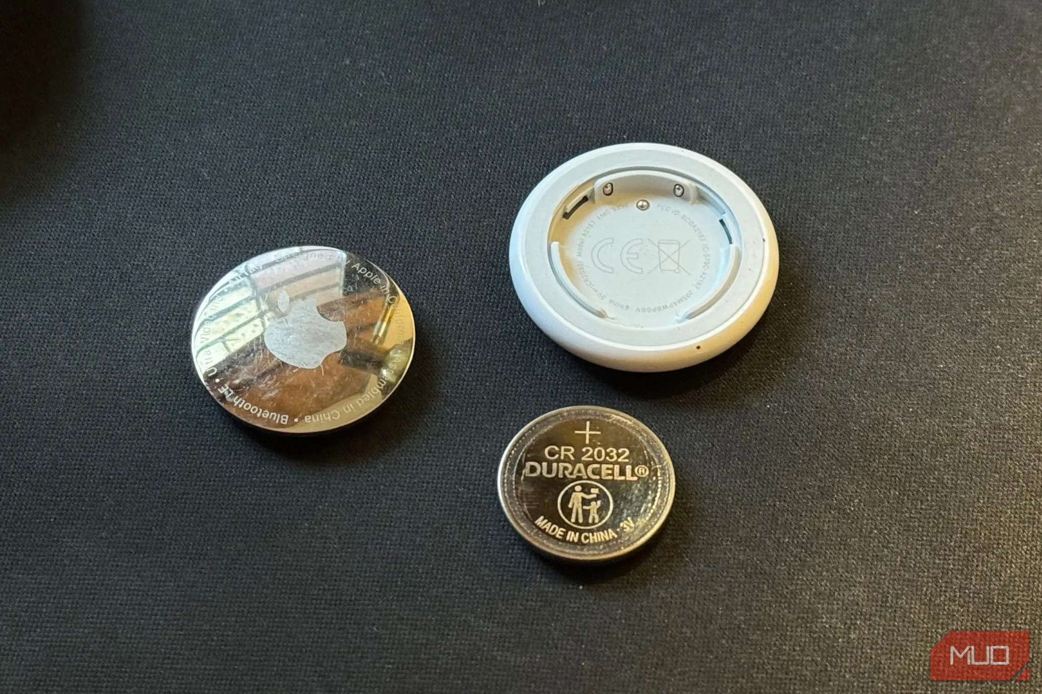A disassembled AirTag placed on a black mat along with its CR 2032 cell