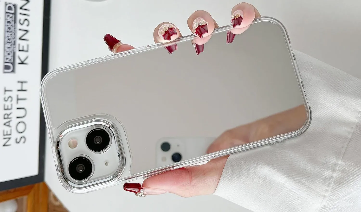 Bàn tay đang cầm một chiếc iPhone có ốp lưng tráng gương, biến mặt lưng điện thoại thành một chiếc gương nhỏ tiện lợi