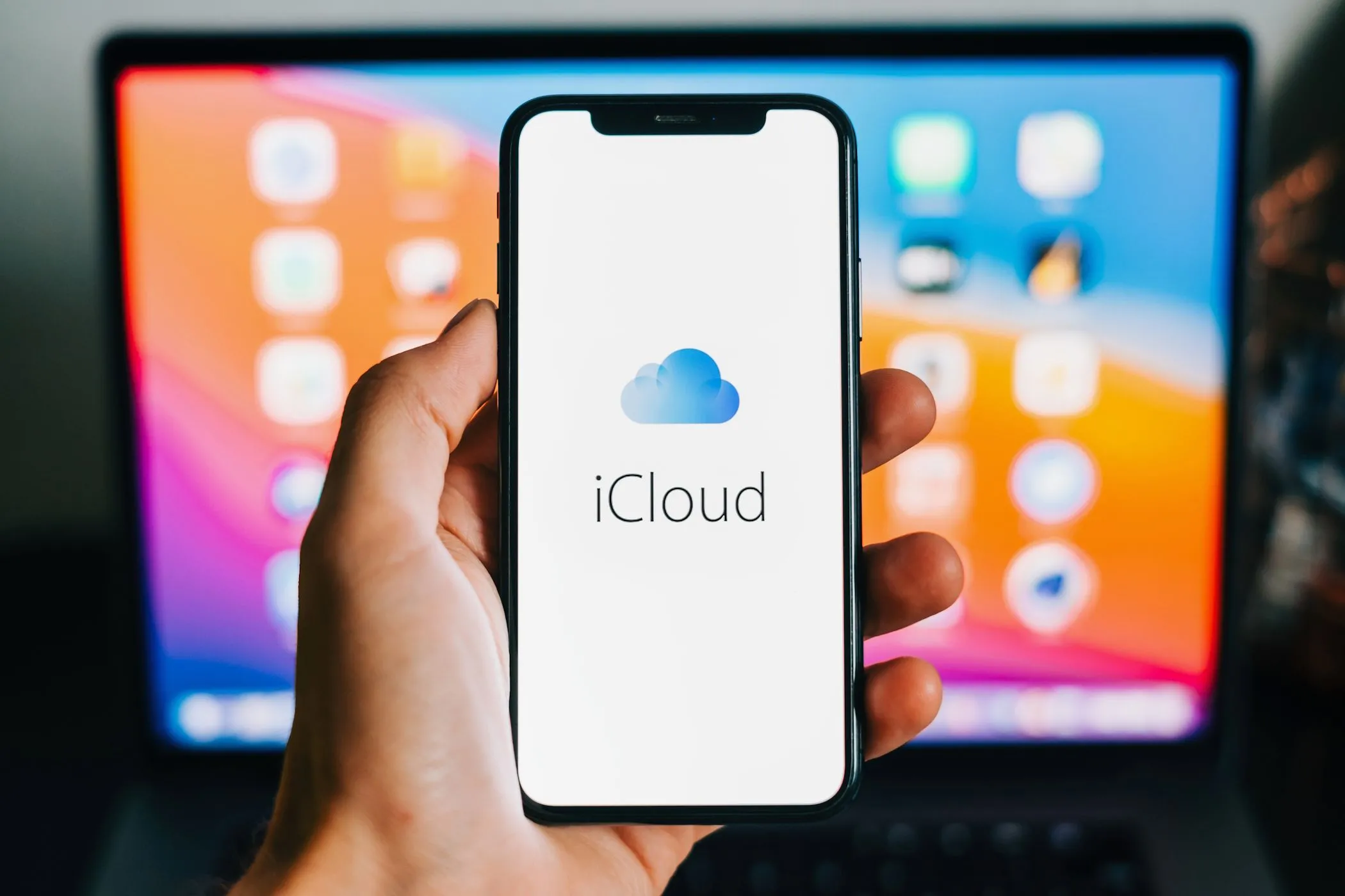 Biểu tượng iCloud trên màn hình iPhone, phía sau là MacBook, thể hiện sự liên kết giữa các thiết bị Apple.