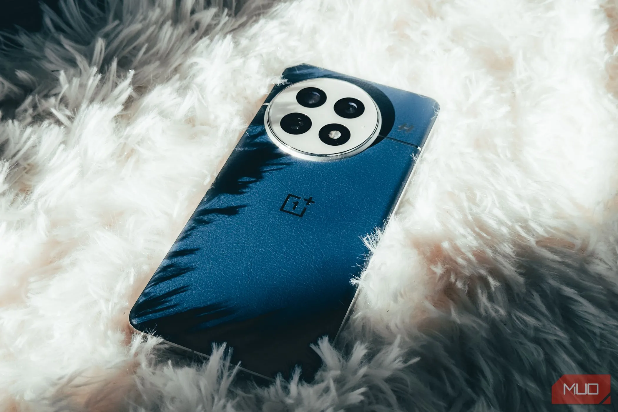 Điện thoại OnePlus 13 màu xanh Midnight Ocean với mặt lưng da vegan mềm mại đặt trên thảm trắng