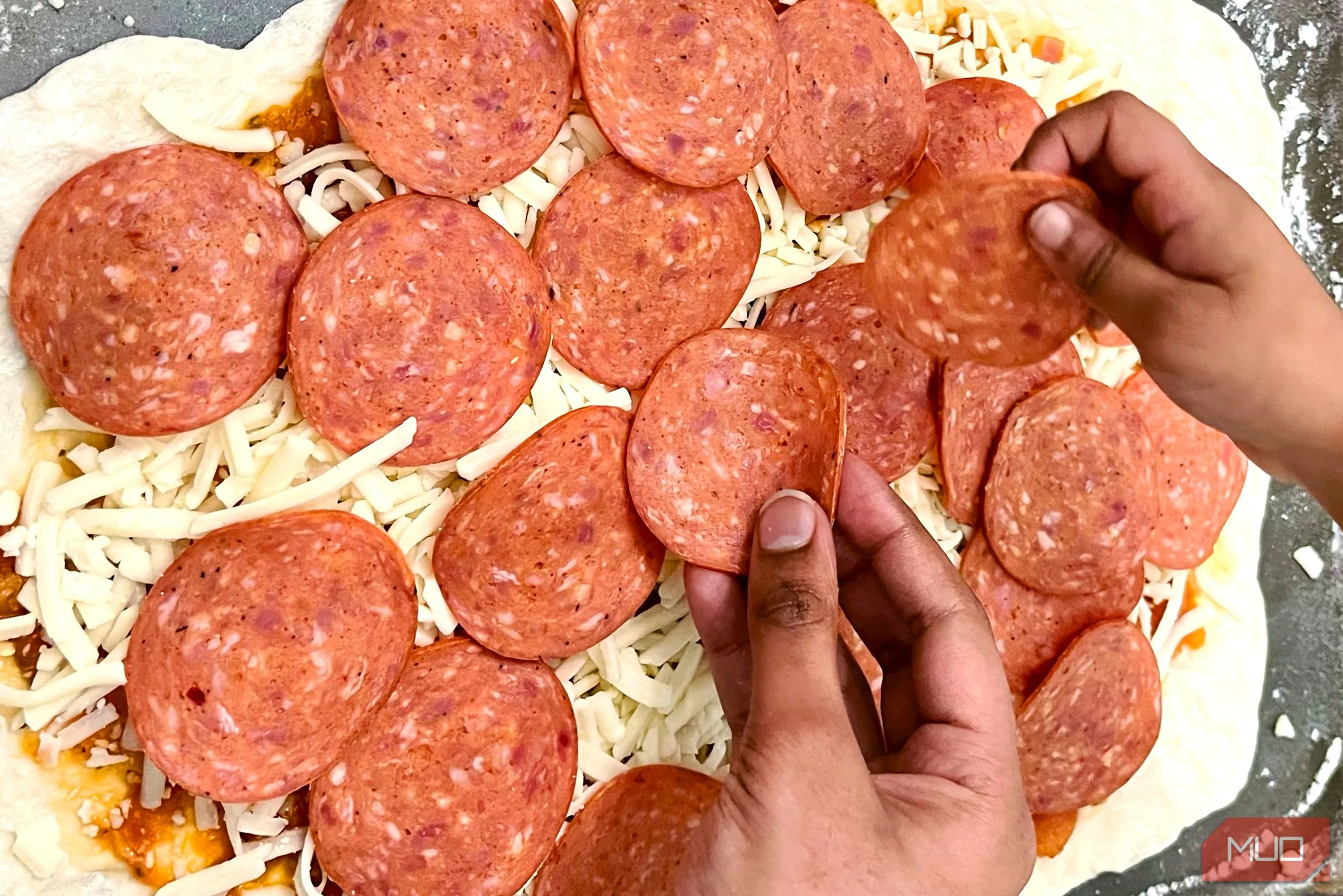 Đôi bàn tay đang rải nguyên liệu lên đế bánh pizza, tạo nên câu chuyện về quá trình chuẩn bị món ăn