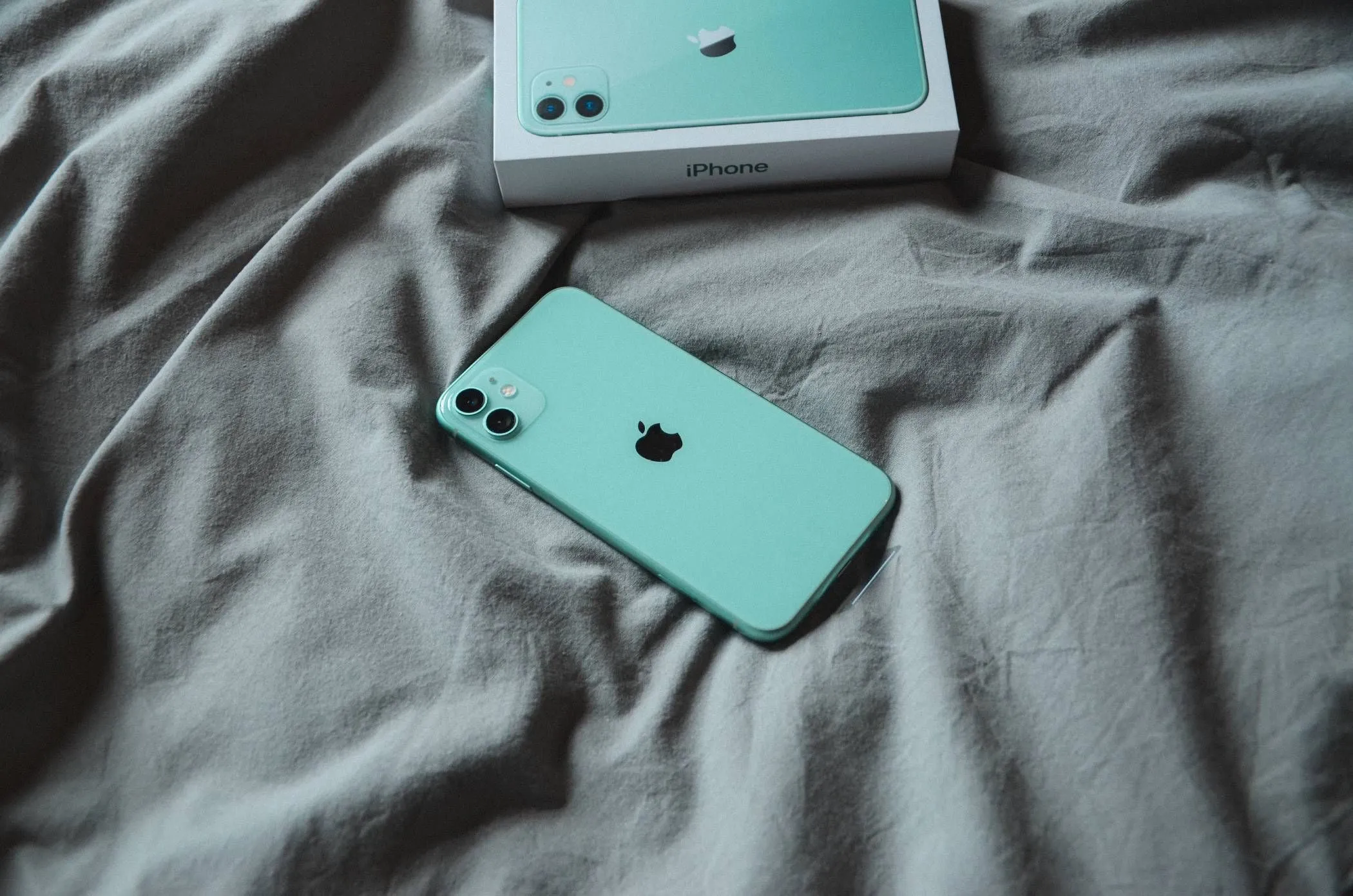iPhone nằm trên chăn ga trải giường màu trắng