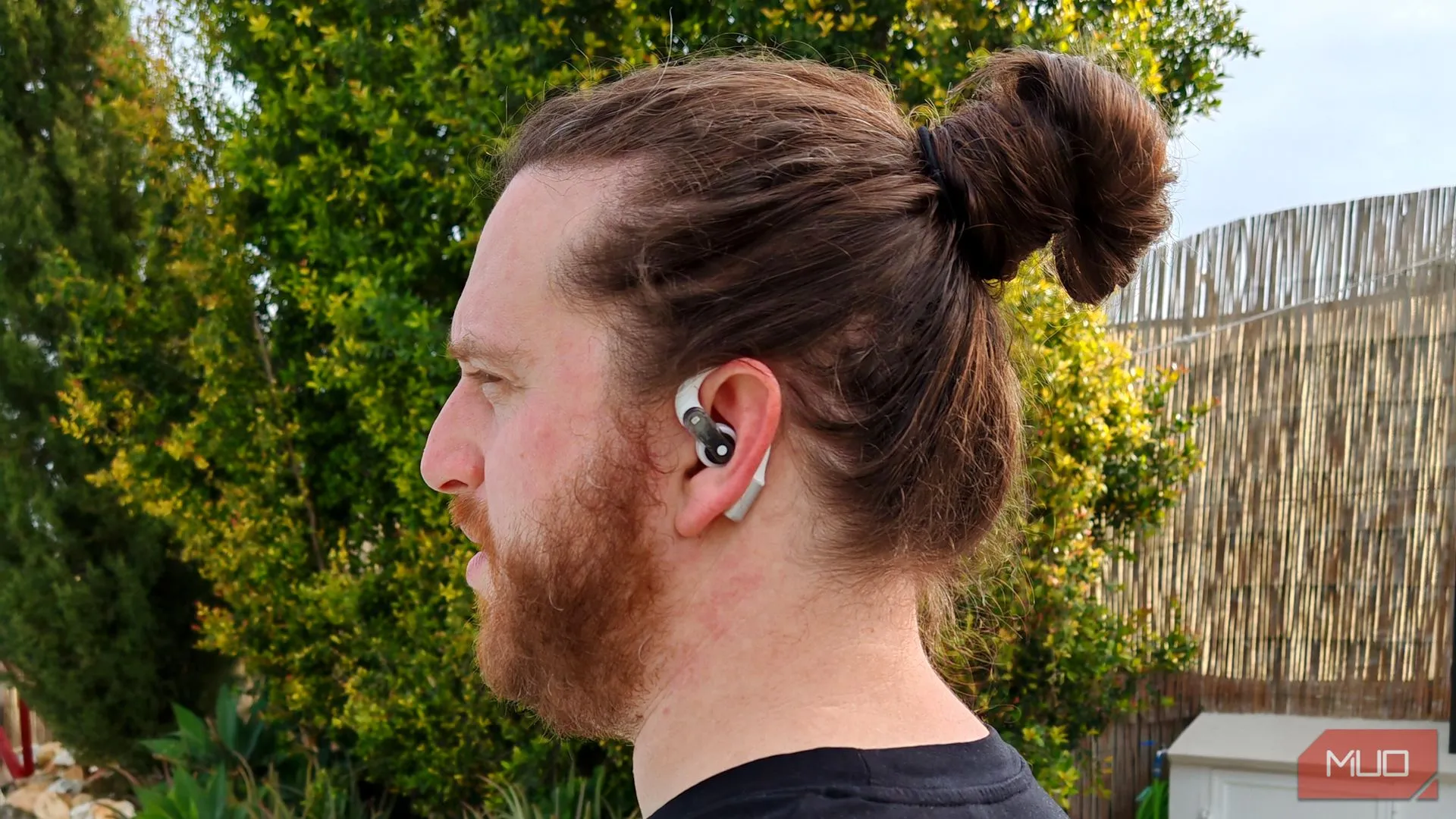 Một người đàn ông đang đeo tai nghe earbuds dạng mở ở tai trái, tập trung vào trải nghiệm nghe nhạc với chất lượng âm thanh chi tiết.