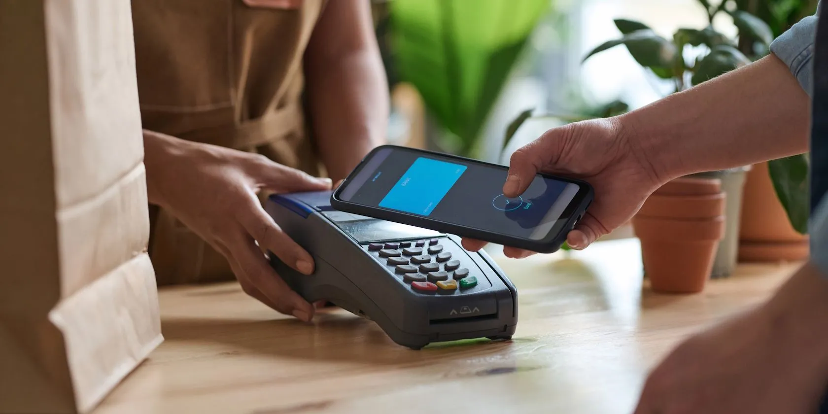 Một người đàn ông đang thực hiện thanh toán không tiếp xúc bằng điện thoại thông minh qua chip NFC tại quầy thu ngân cửa hàng tạp hóa