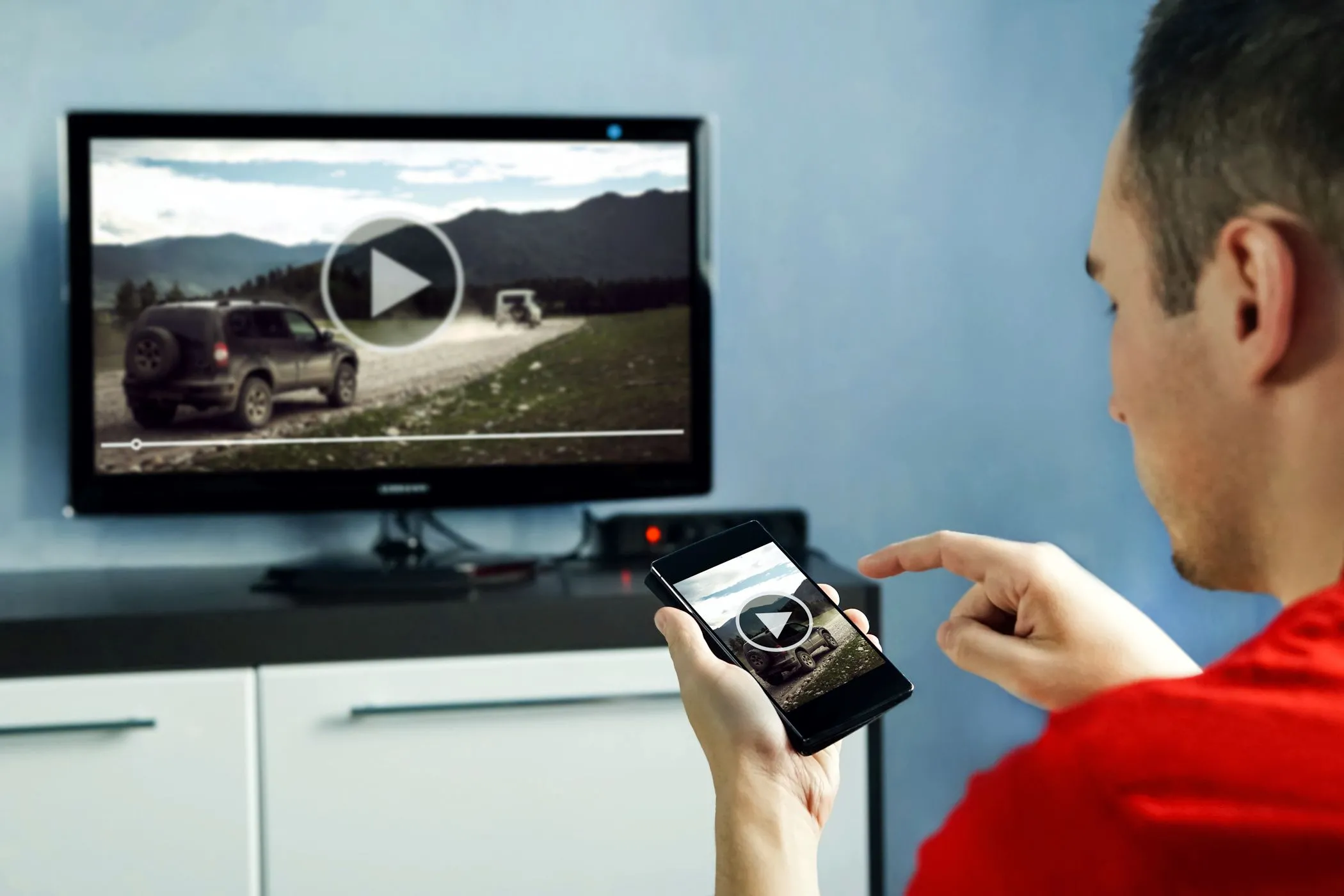 Người đàn ông xem video trên Smart TV và sử dụng ứng dụng điều khiển trên điện thoại