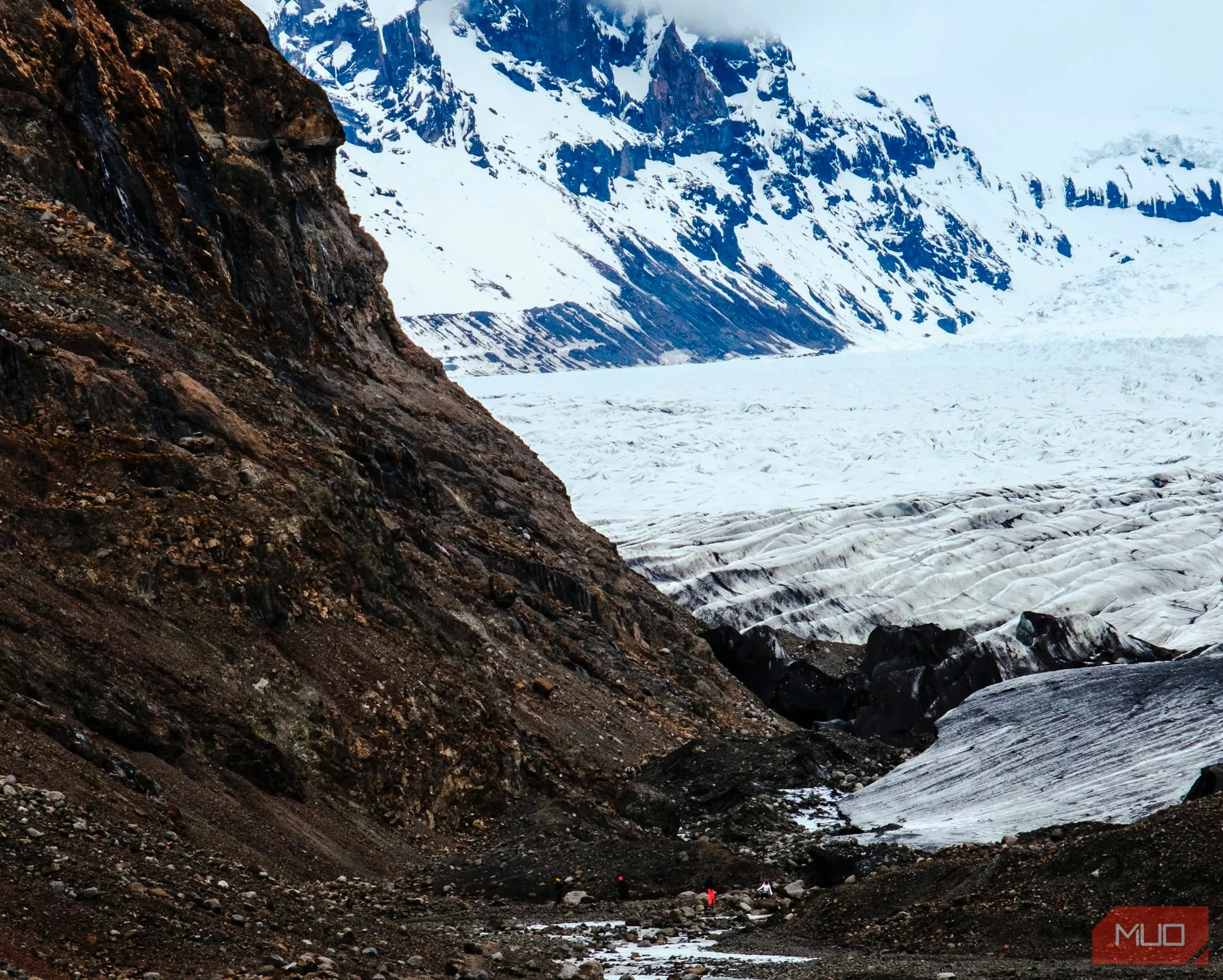 Người leo núi nhỏ bé giữa khung cảnh sông băng và núi non hùng vĩ tại công viên quốc gia Iceland, thể hiện quy mô và chi tiết nhỏ của dòng suối.