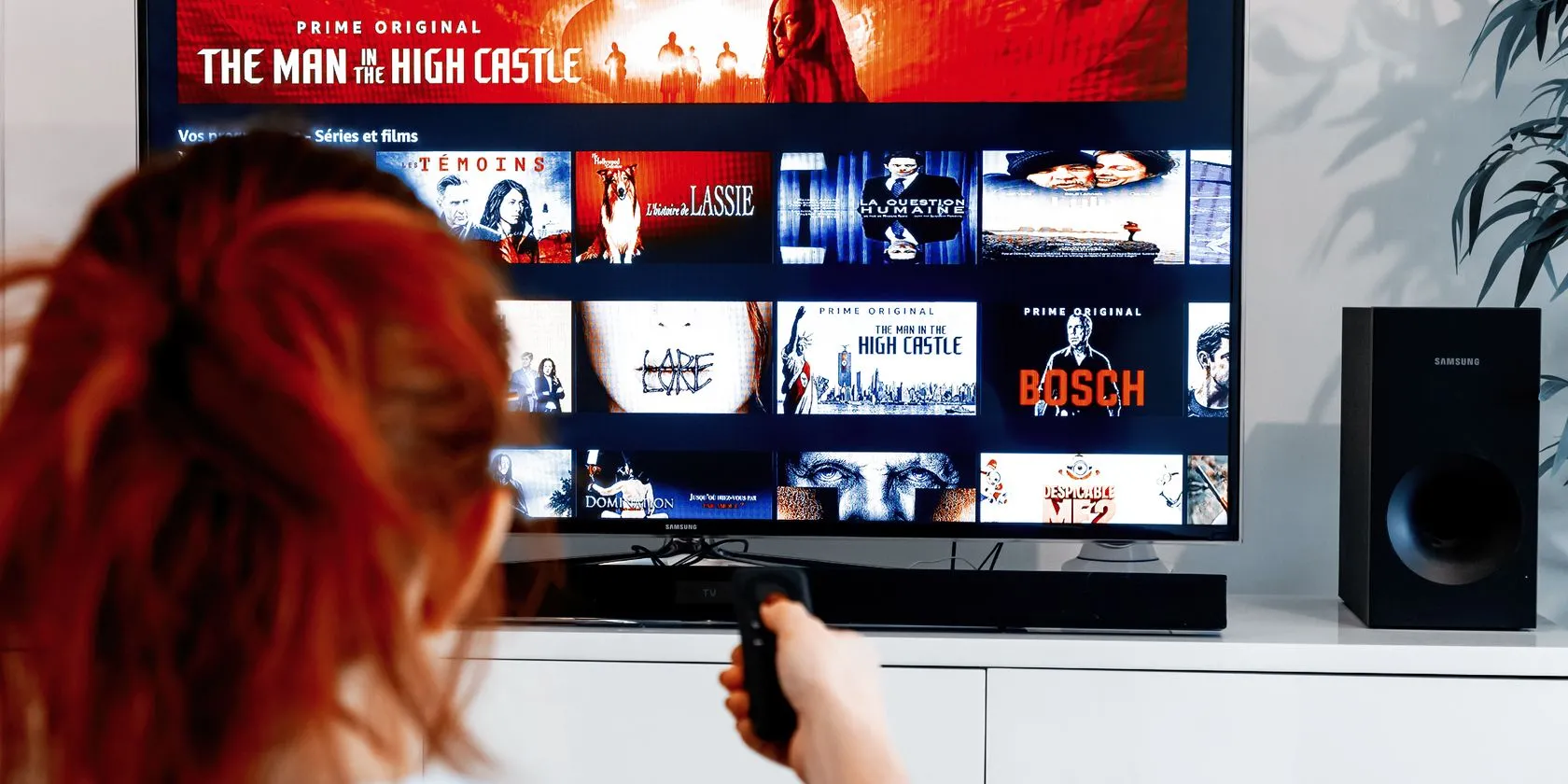 Người phụ nữ đang sử dụng điều khiển từ xa với màn hình hiển thị Amazon Prime Video, minh họa việc truy cập nhanh thông tin