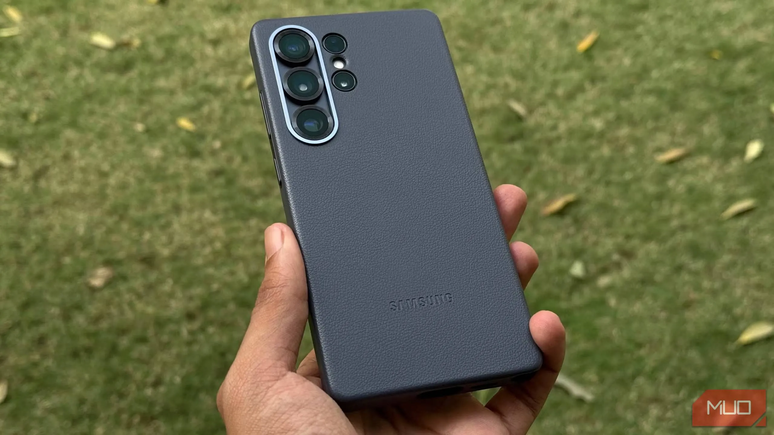 Ốp lưng Kindsuit màu đen trên Galaxy S25 Ultra được giữ trong tay, phía sau là bãi cỏ