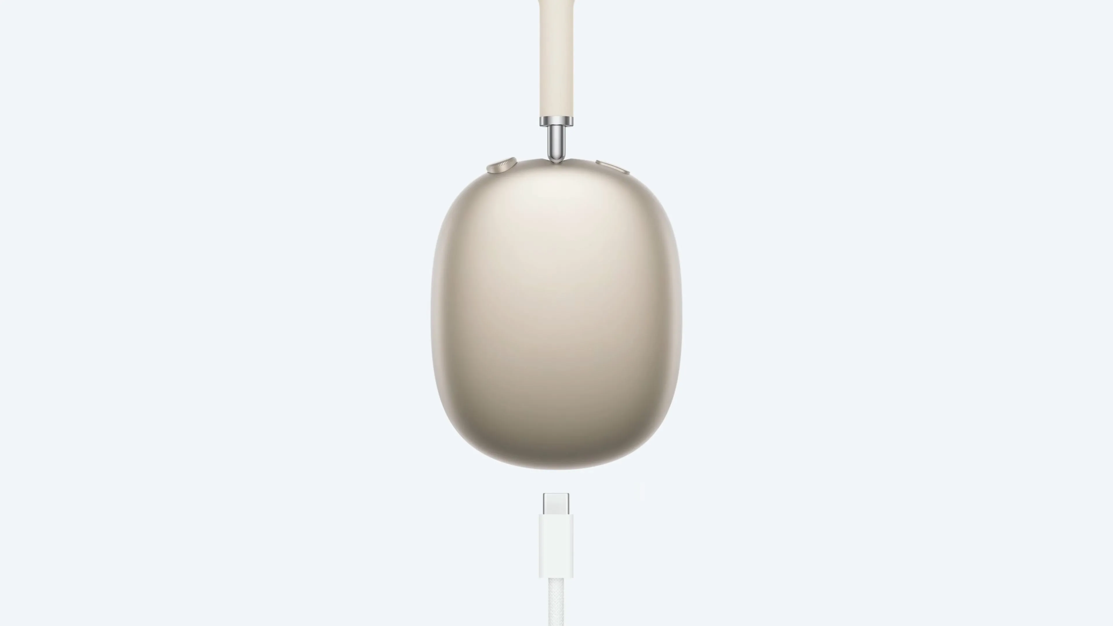 Tai nghe AirPods Max màu Starlight đang sạc với cáp USB-C, minh họa việc không thể vừa sử dụng vừa sạc